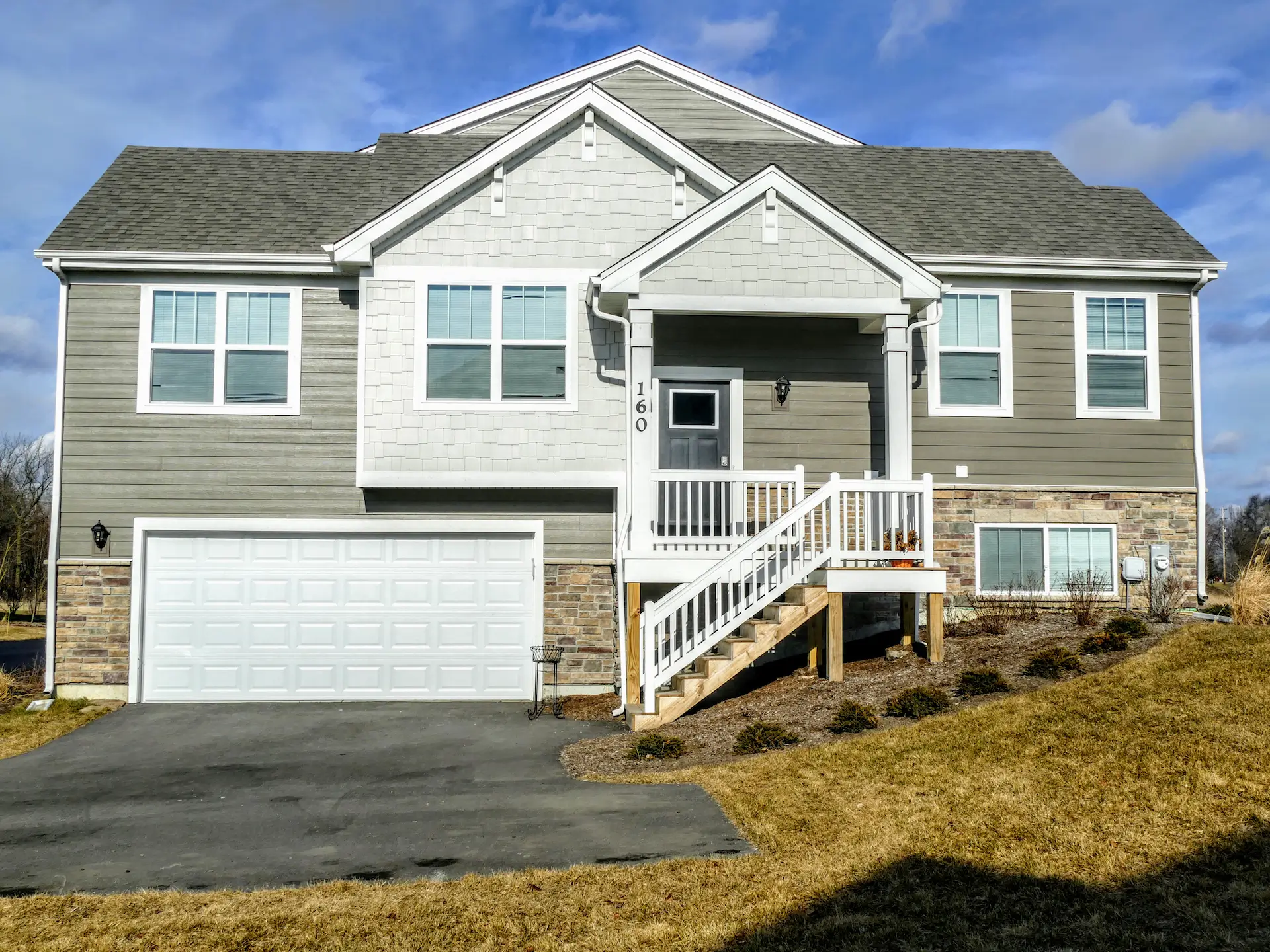 Standalone townhome with a mix of green siding, beige stone, and white trim with a short staircase leading to the front patio just to the top right of the garage.