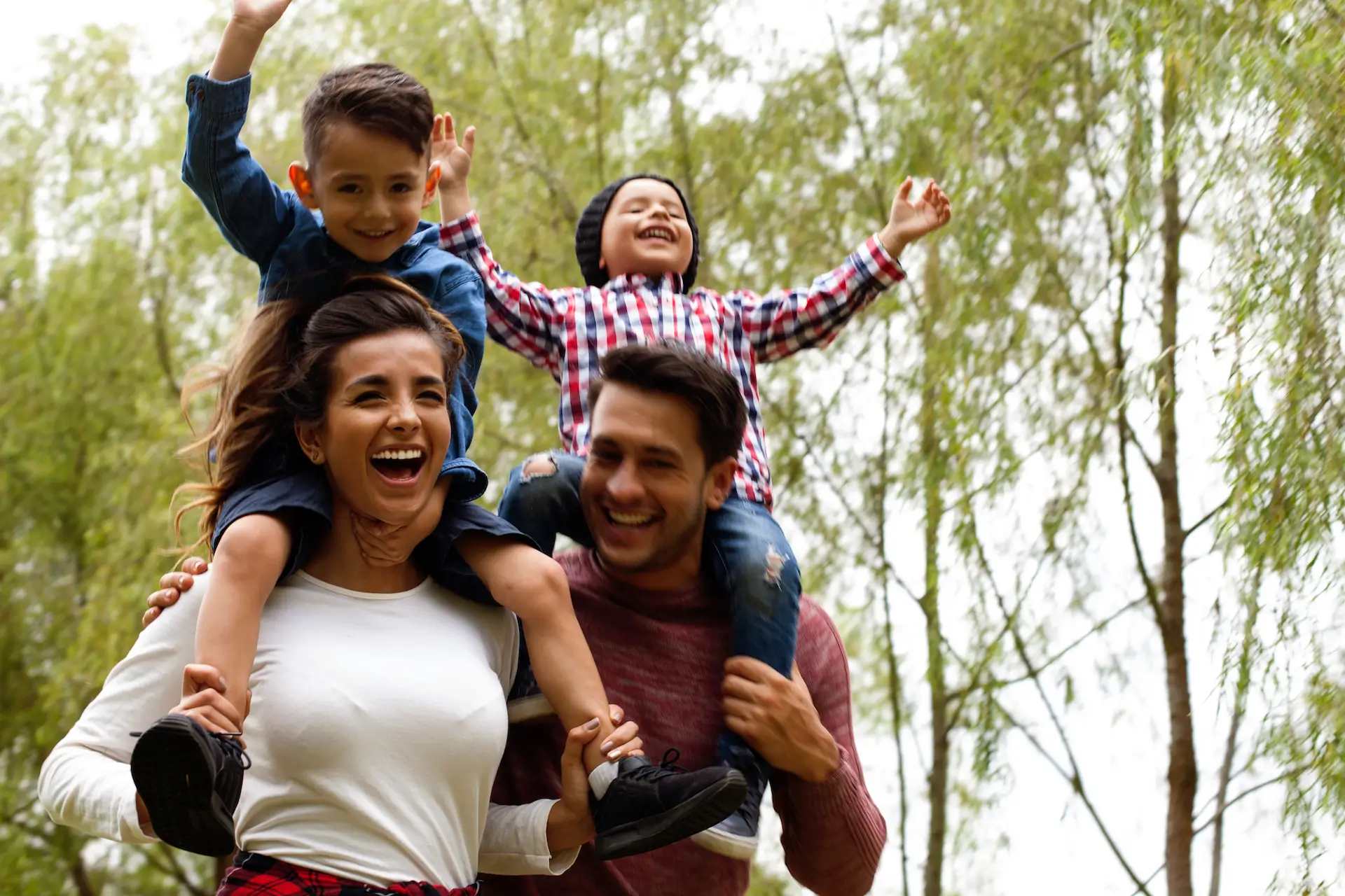 Young man and woman laughing and running outside with their kids on their shoulders