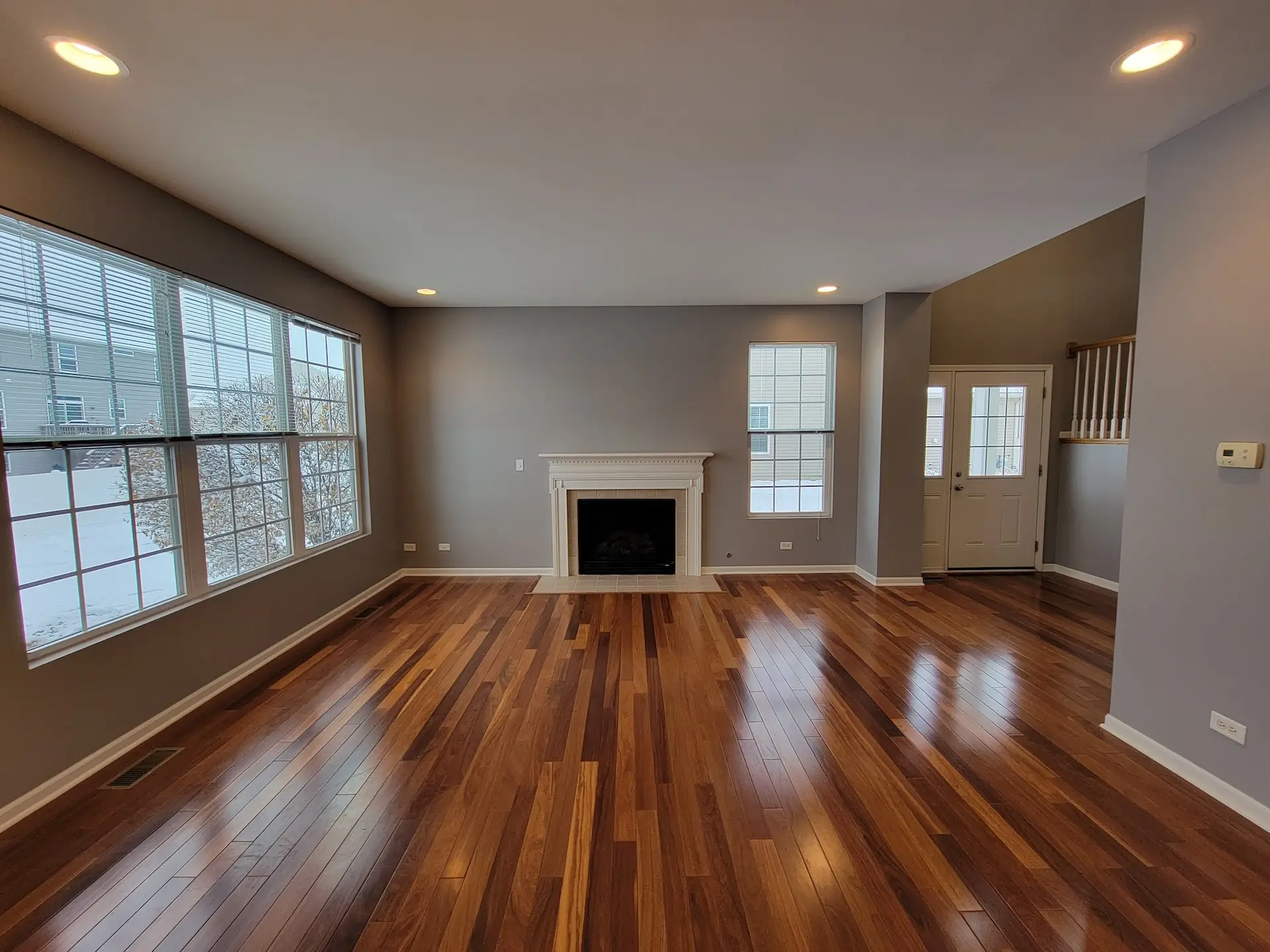 living room with four large windows, multi-shade brown wood style flooring, gray walls, a fireplace, and recessed can lighting.