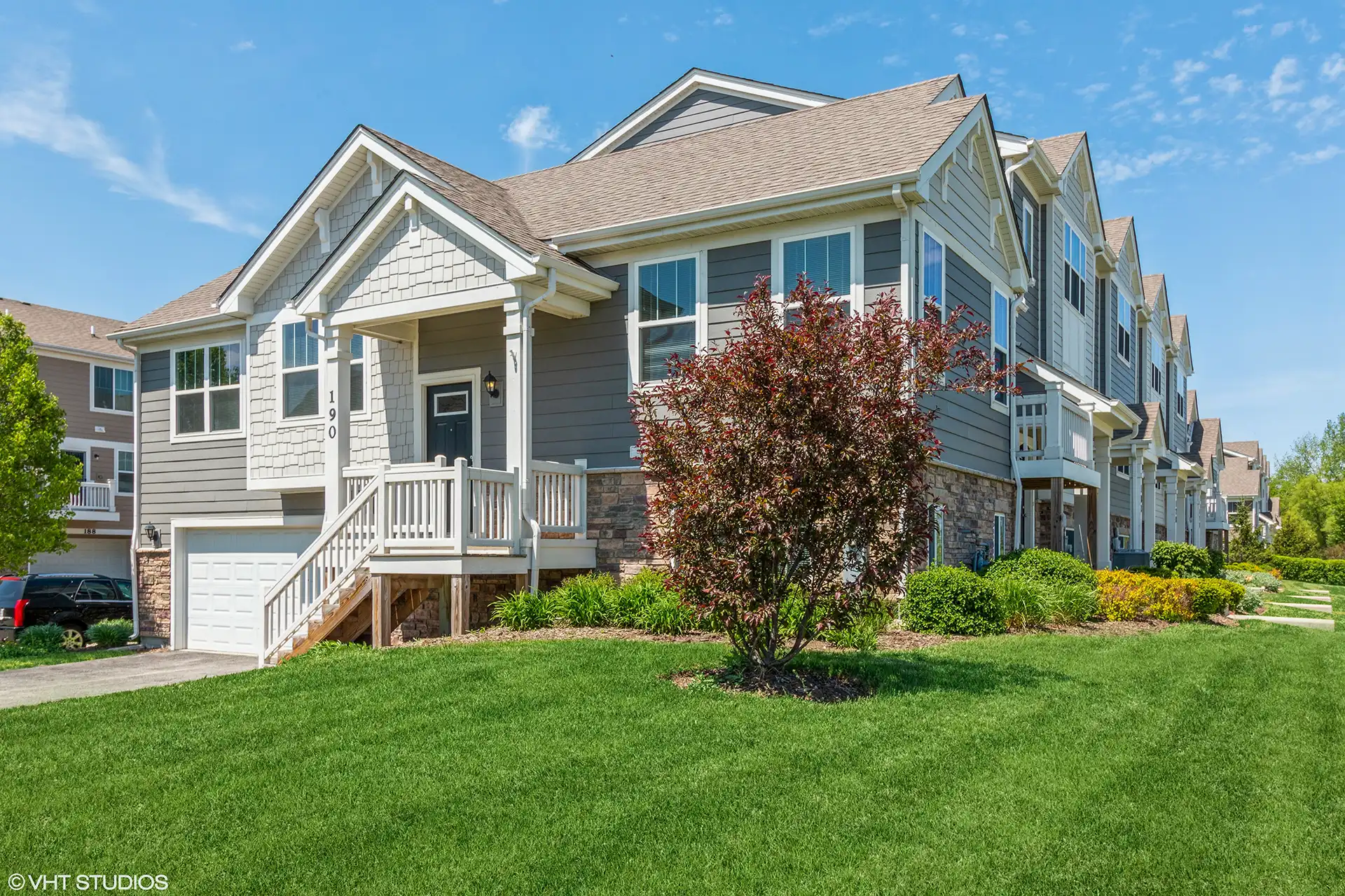 row of split-level townhomes with garages, a large green lawn, and side entry on the end.