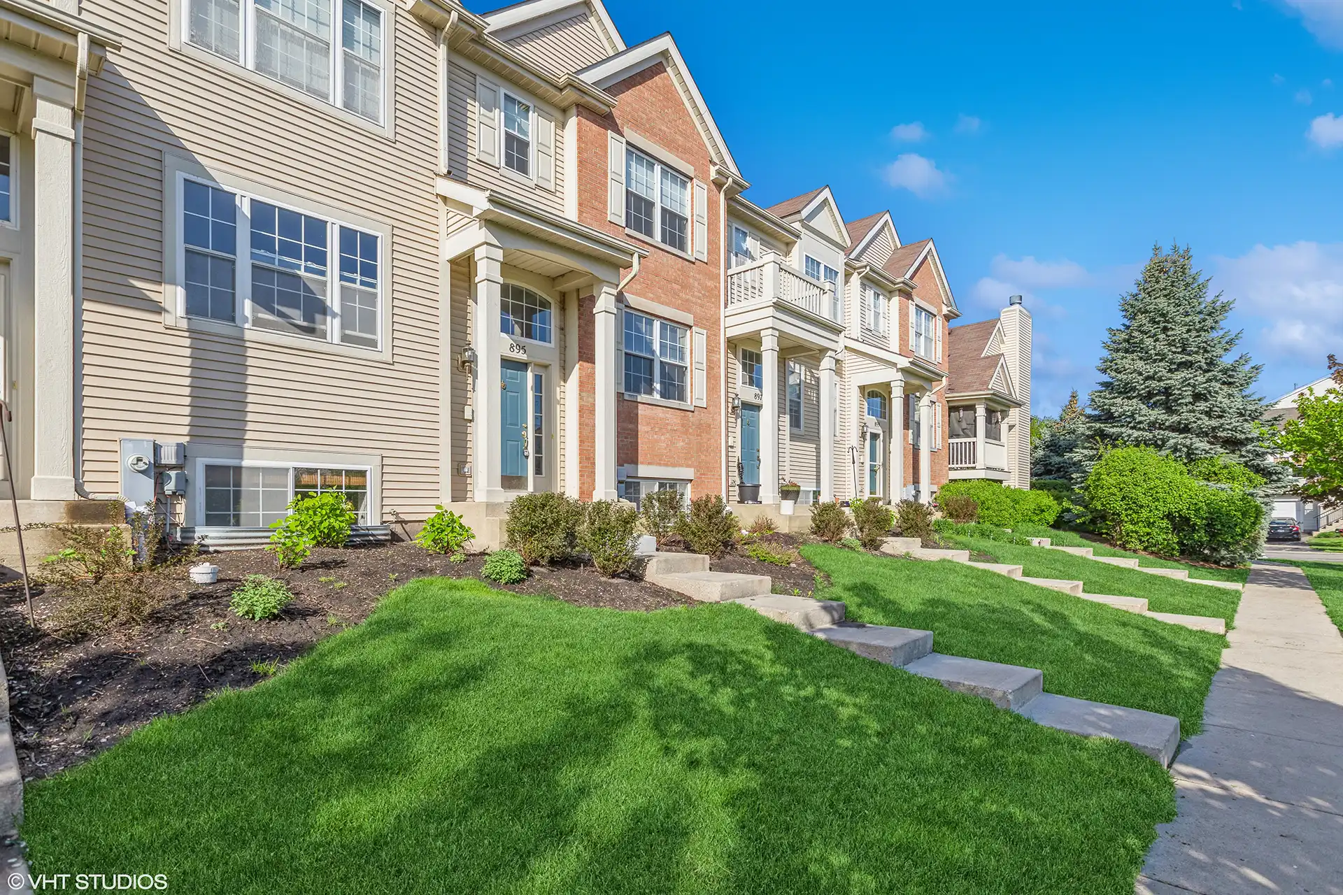 Row of townhomes with green lawns and cement steps leading from paved sidewalk to the front doors.