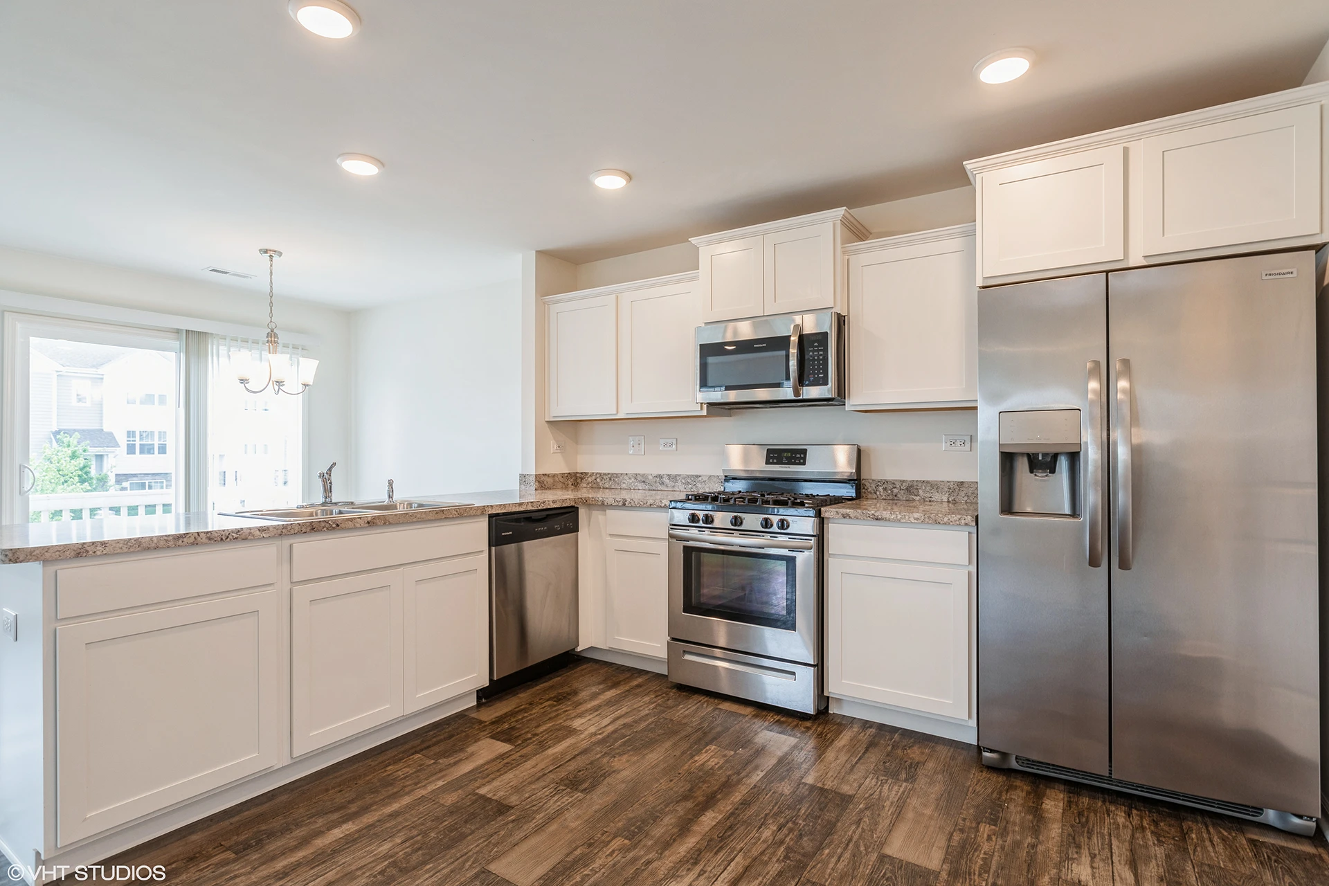 large open kitchen with white wood cabinets, stainless appliances, gas stove, narrow accordion door pantry, and granite pattern laminate countertops.