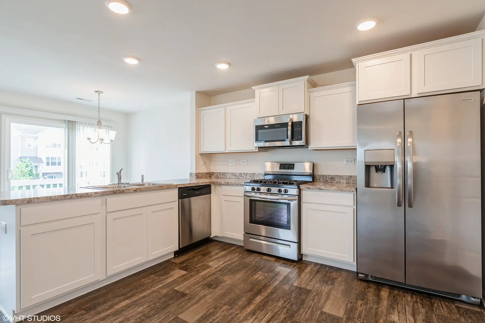 large open kitchen with white wood cabinets, stainless appliances, gas stove, a large bar area with double sink, and adjacent dining and living space.