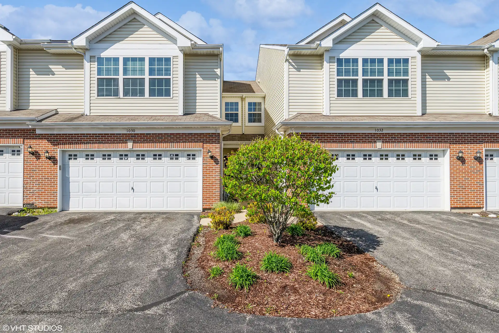 driveways leading to townhome row garages with red brick on bottom and cream wood siding on top level.