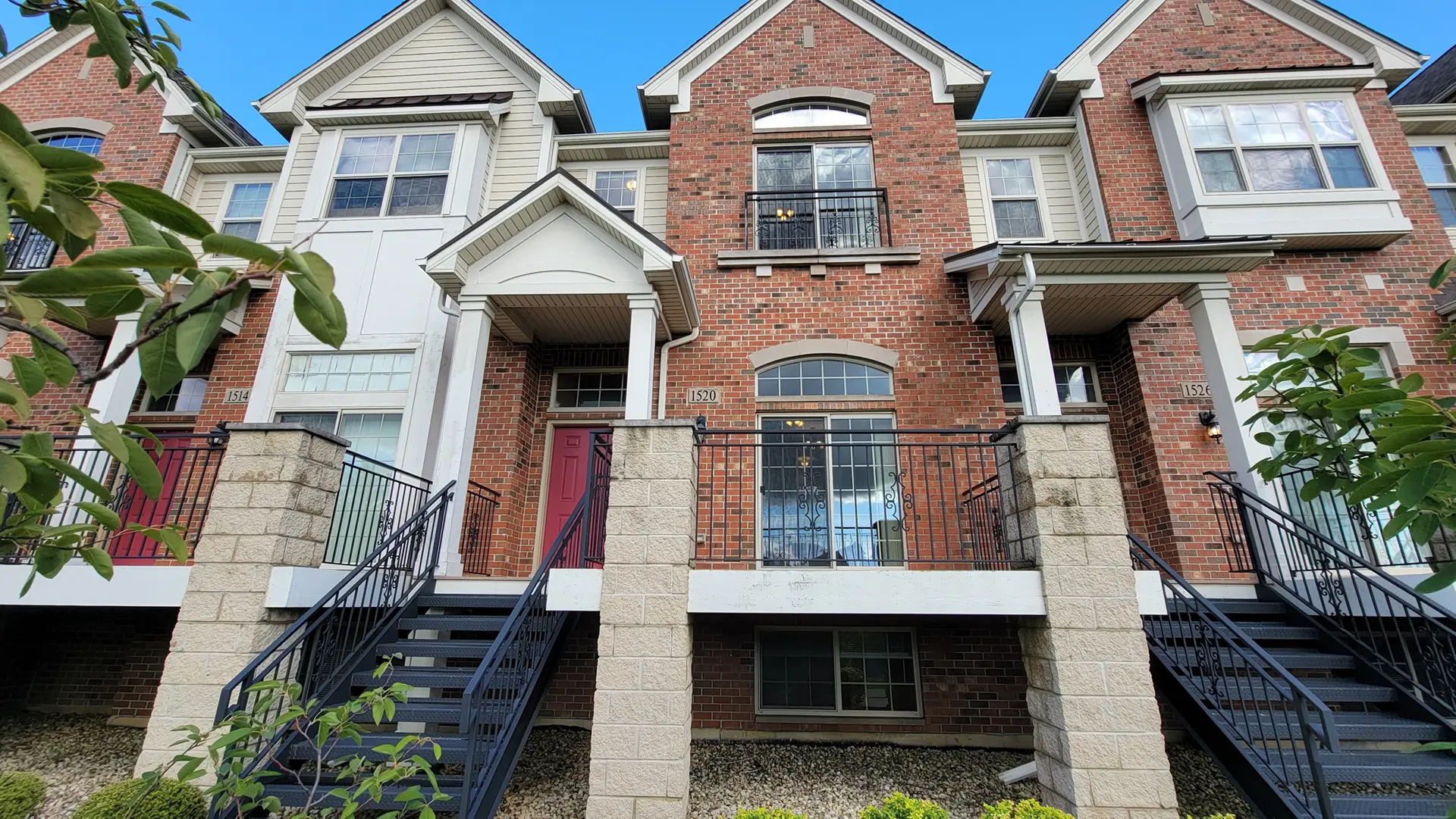 Row of multi-level townhomes with red brick and white wood siding. Black metal stairs lead to the front door landings.