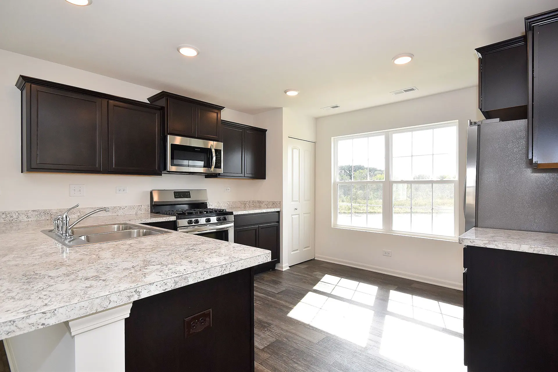 large open kitchen with dark wood cabinets, stainless appliances, gas stove, a large bar area with double sink, and granite pattern laminate countertops.